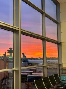 looking out an airport window at plane and sunset