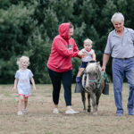 Grandparents helping a young boy ride a pony.